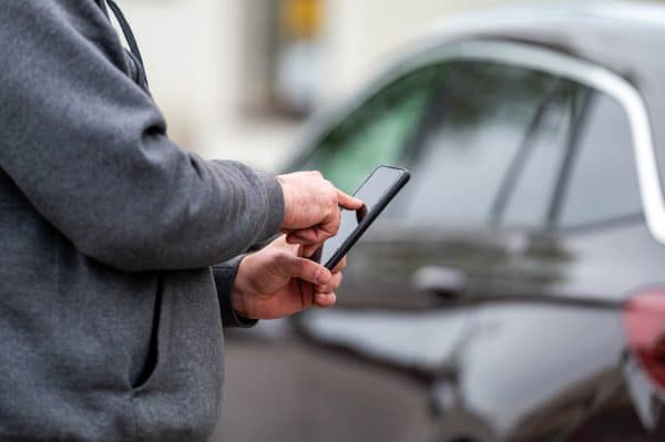 man with smartphone standing next to the car, using mobile app for online communication, shpping